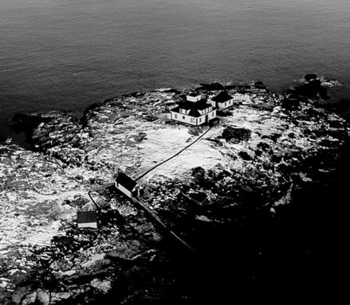 Aerial black and white photo of a Egg Rock lighthouse on rocky coastal terrain beside the ocean in Maine